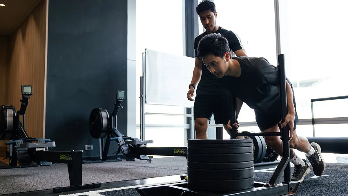 A Virgin Active trainer coaching a member through a sled push
