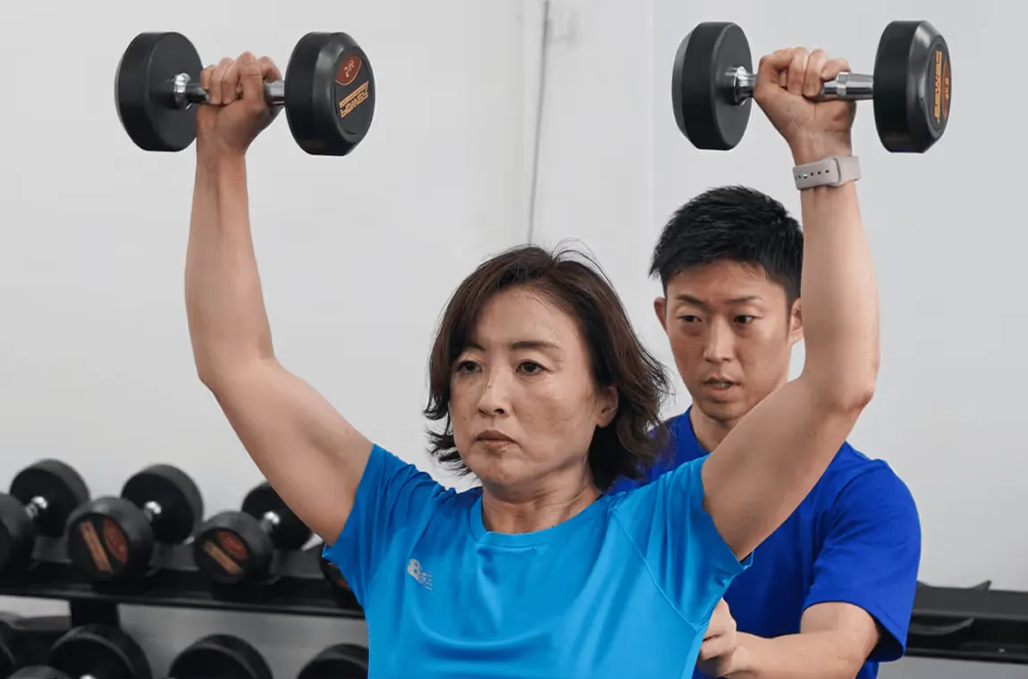 A We'll Go trainer guiding a client through a dumbbell shoulder press